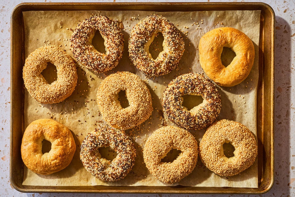 Various bagels on a sheet of parchment atop a baking pan fresh out of the oven.