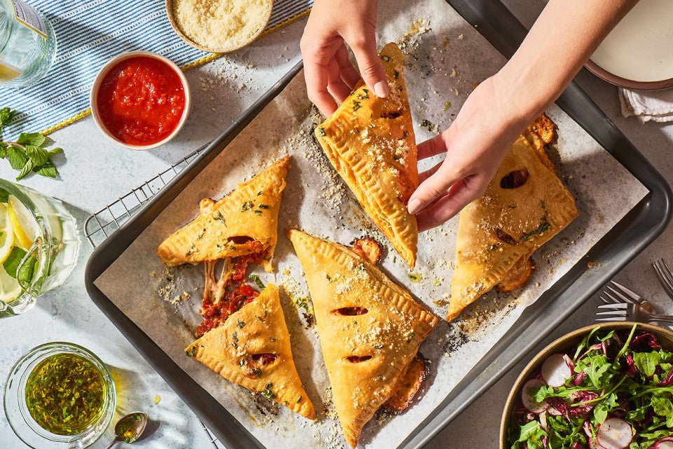 Flaky Puff Crust Pizza Turnovers on a baking sheet with someone lifting one up