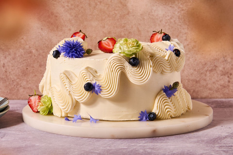 A cake frosted with Italian Buttercream and adorned with flowers, fruits and berries