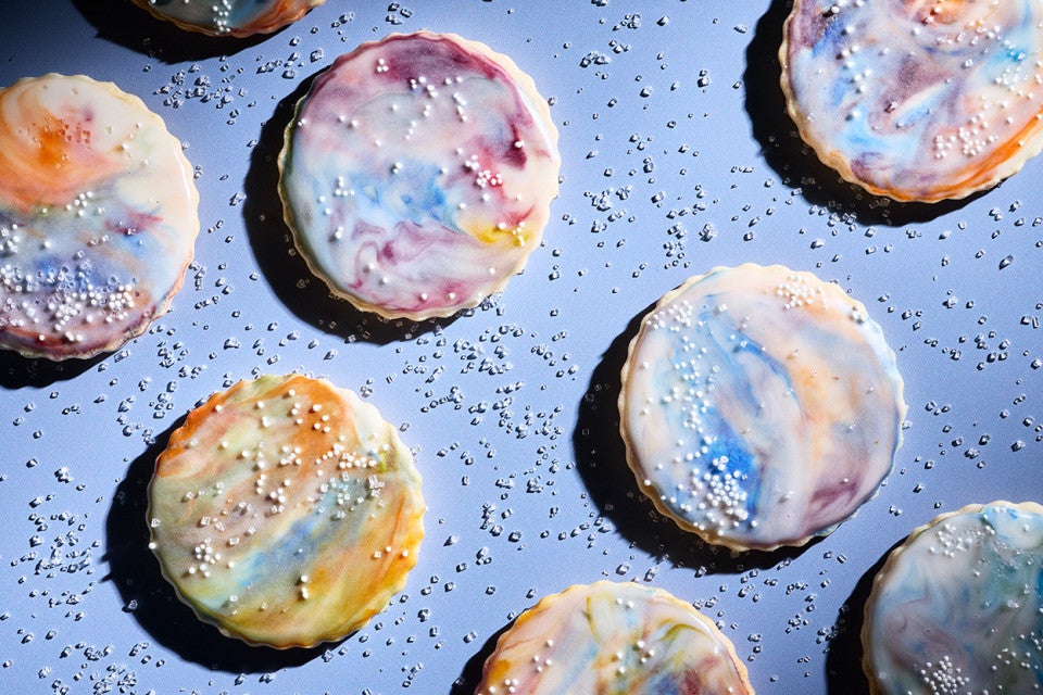Northern Lights Iced Sugar Cookies arranged on a blue background surrounded by sprinkles of sparkling sugar