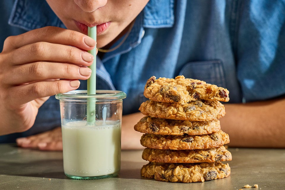 Drinking from a glass of milk that is sitting next to a stack of The Softest Oatmeal Raisin Cookies