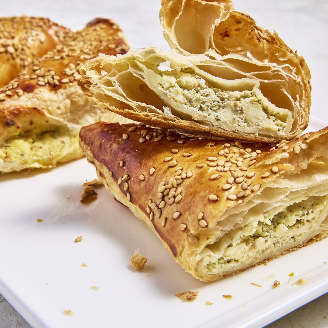 Cross section of boureka showing laminated layers of sesame coated pastry and filling.