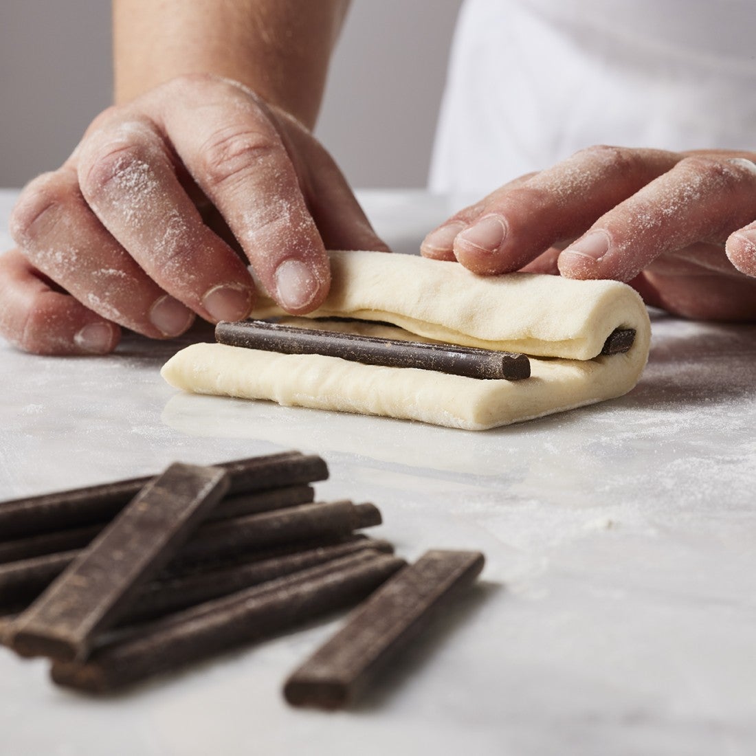 Hands preparing croissants by rolling chocolate into raw layered pastry dough.