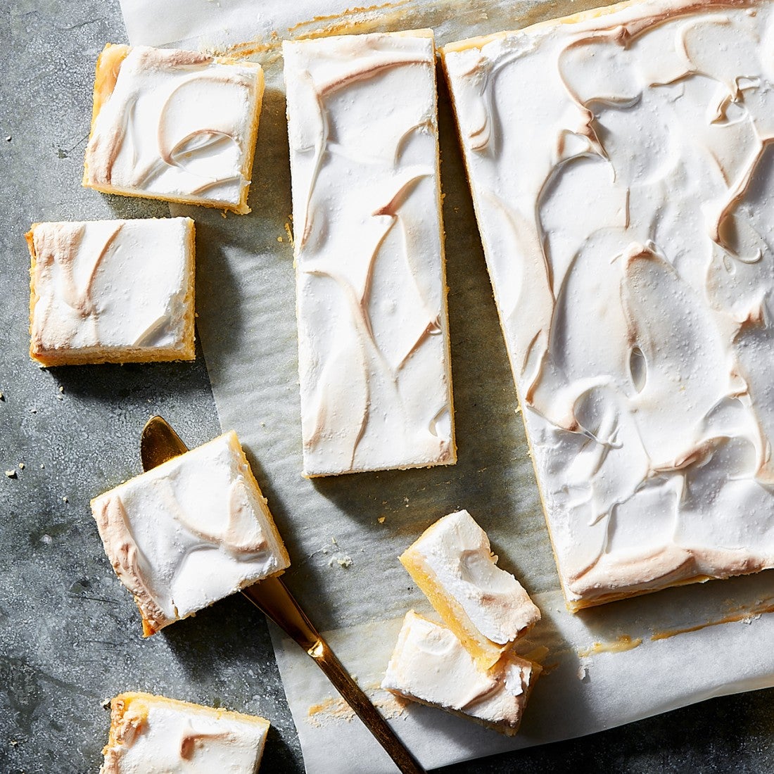 Overhead photograph of lemon meringue bars with various shapes sliced and scatter on a counter.