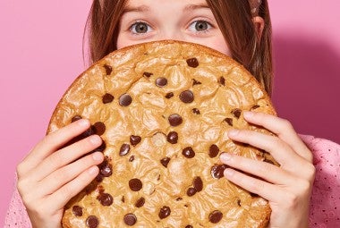 A young girl hiding behind a Chocolate Chip Skillet Cookie