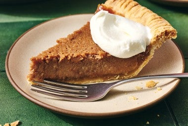 Slice of smooth boiled apple cider pie shown from the side and topped with a dollop of whipped cream.
