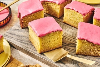 Cranberry-Orange Olive Oil Cake sliced up and arranged on a glass plate with a gold hued serving spatula under one of the golden slices.