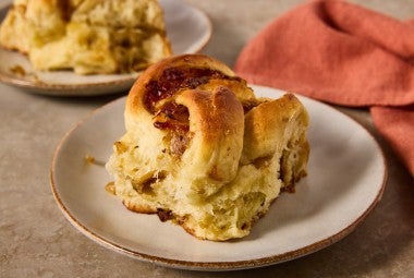 A French Onion Roll on a plate showing the golden brown exterior and lofty baked interior with caramelized onions.
