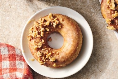 A Maple Donut on a plate with half coated in broke nut meat and the other half glazed.