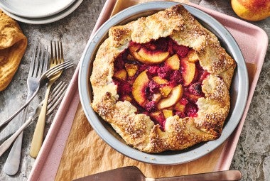 Photograph of Rustic Raspberry-Peach Pie from above with a perfectly browned folded crust around the edges of a vibrant raspberry and peach filling.