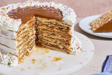 Torta Chilena photographed from the side showing a generous slice removed with layers of dulce de leche, crispy pastry, and creme fraiche frosting.