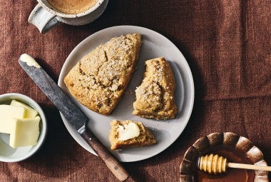 Two Golden Wheat Scones on a plate, one unbroken, the other broken with a dollop of butter on it.