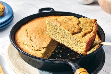 A slice of Sourdough Cornbread being removed from a cast iron skillet.