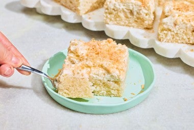 A slice of Creamy Coconut Sheet Cake on a plate with a bite on a fork