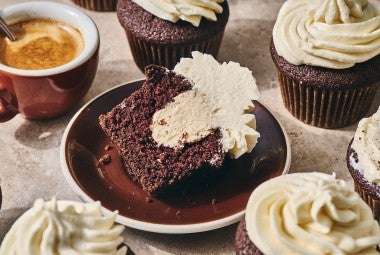 Irish Cream Cupcake on a plate with other cupcakes and a cup of coffee in the photo.
