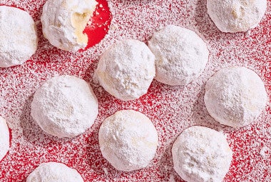 Lemon Snowball Cookies coated in powdered sugar on a red surface