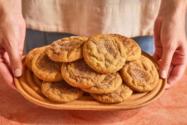 Pumpkin Snickerdoodle Cookies stacked and arranged on a plate with someone holding the plate up